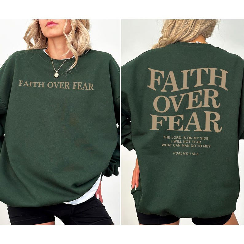 May include: A dark green sweatshirt with the text "FAITH OVER FEAR" printed on the front and back. The back also includes the text "THE LORD IS ON MY SIDE: I WILL NOT FEAR WHAT CAN MAN DO TO ME? PSALMS 118:6".
