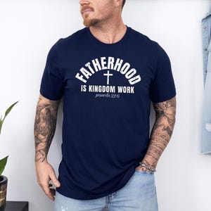 Pu&ograve; includere: T-shirt blu navy con testo bianco: "FATHERHOOD IS KINGDOM WORK" e "proverbi 22:6" con una croce. La maglietta &egrave; a maniche corte.
