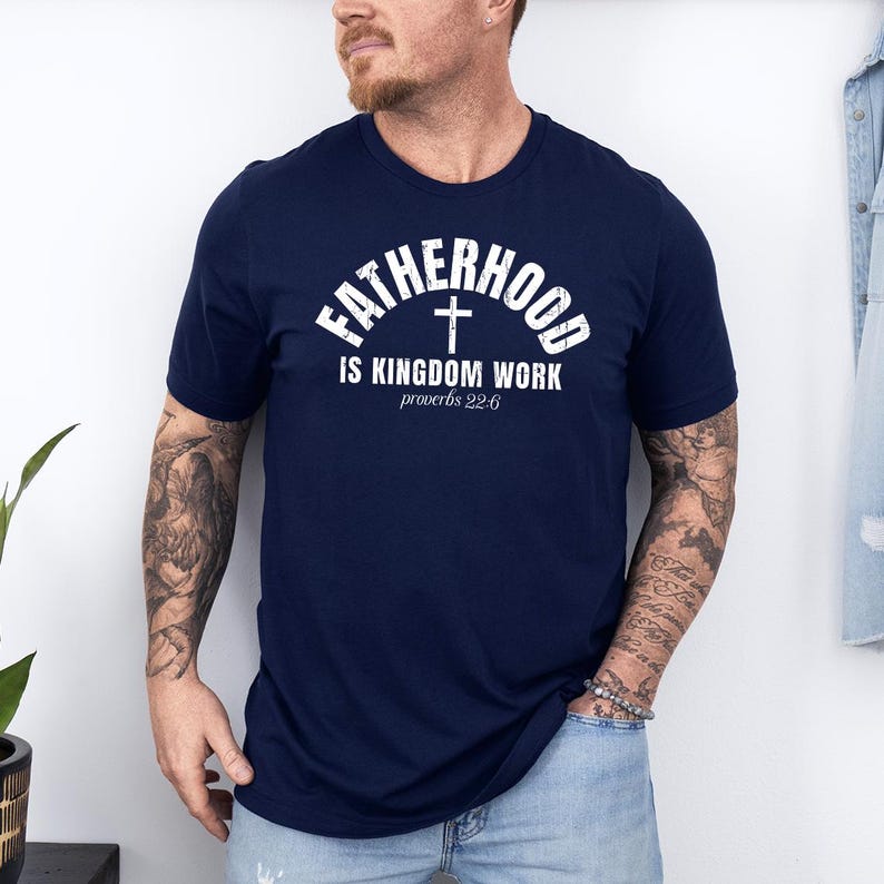 Pu&ograve; includere: T-shirt blu navy con testo bianco: "FATHERHOOD IS KINGDOM WORK" e "proverbi 22:6" con una croce. La maglietta &egrave; a maniche corte.