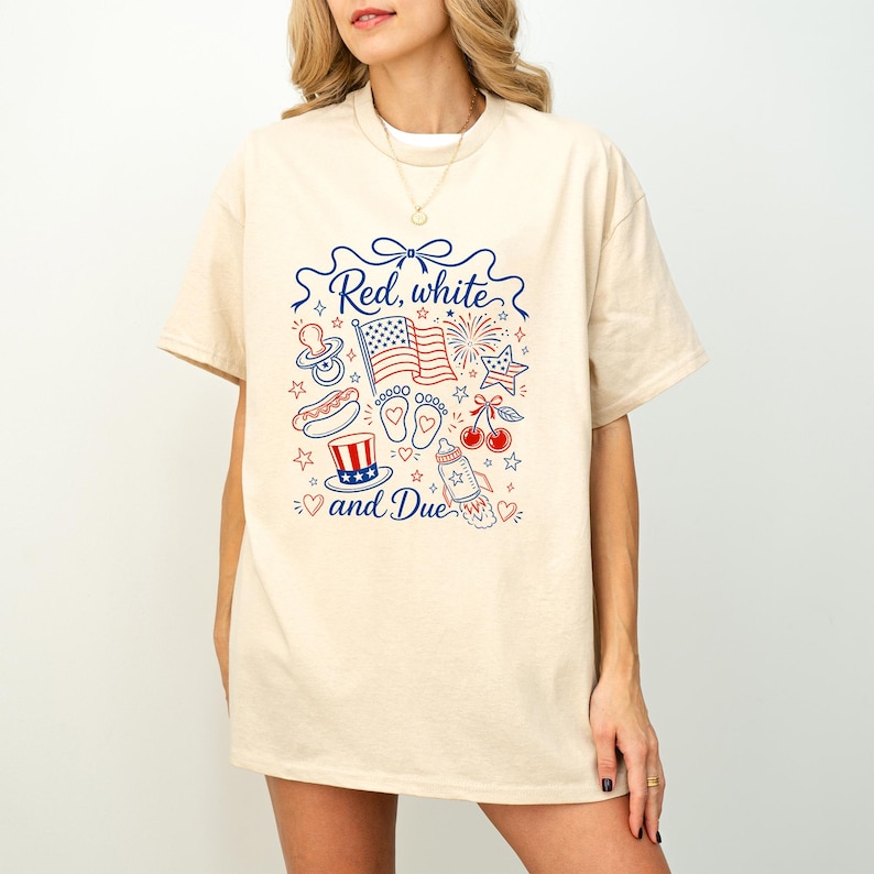 May include: Cream-colored t-shirt with a patriotic design in red and blue. The design includes an American flag, fireworks, a baby bottle, and the text "Red, white and Due".