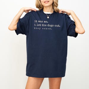 May include: Navy blue t-shirt with the text "it was me. i let the dogs out. they asked." in white. The shirt has a crew neck and short sleeves. The shirt is made of a soft material.