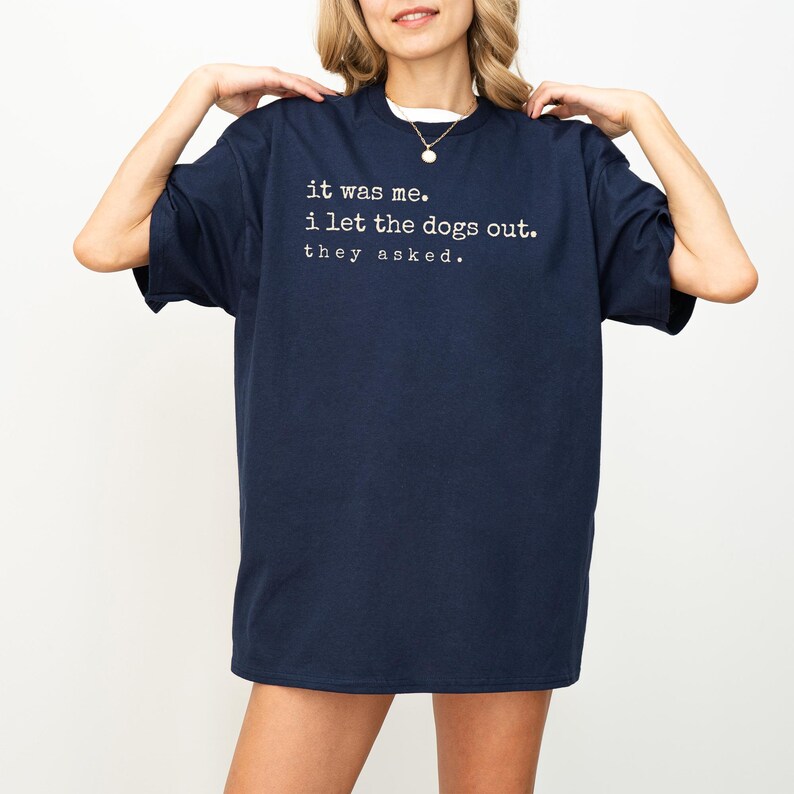 May include: Navy blue t-shirt with the text "it was me. i let the dogs out. they asked." in white. The shirt has a crew neck and short sleeves. The shirt is made of a soft material.