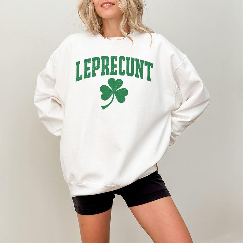 May include: White sweatshirt with the word "LEPRECONT" in green block letters and a green shamrock graphic. The sweatshirt is a casual style, suitable for St. Patrick's Day or everyday wear.