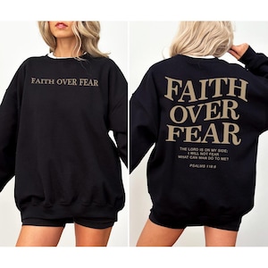 May include: Black sweatshirt with the text "FAITH OVER FEAR" in a tan color on the front and back. The back also includes the Bible verse Psalms 118:6. The sweatshirt has a white collar.