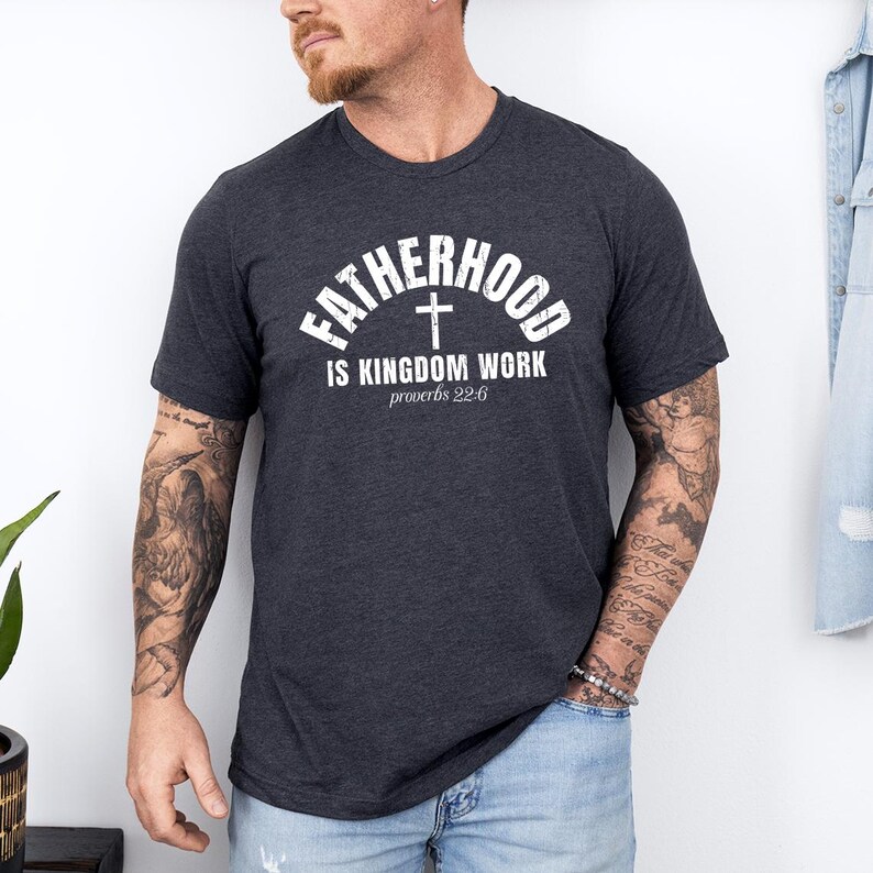 Pu&ograve; includere: T-shirt grigio scuro con la scritta bianca "FATHERHOOD IS KINGDOM WORK" e una croce. Il testo "proverbi 22:6" &egrave; in basso. La maglietta &egrave; a girocollo ed &egrave; realizzata in materiale morbido.
