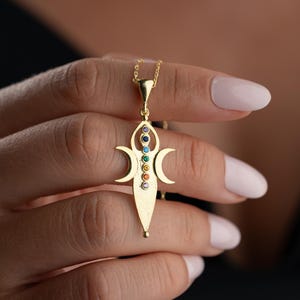May include: A gold-toned pendant necklace featuring a central vertical column of seven small, multi-colored circular gemstones. The pendant design incorporates two symmetrical crescent moon shapes on either side of the central gemstone column.
