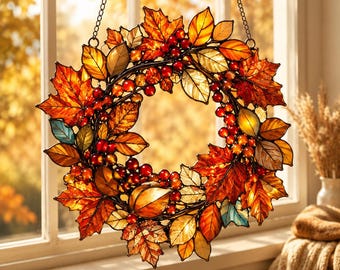 Op de afbeelding: Een ronde glas-in-lood zonnevanger met een verzameling herfstbladeren in tinten oranje, rood, geel en bruin, afgewisseld met trossen kleine rode bessen. Het object hangt aan een dunne metalen ketting om het op te kunnen hangen.