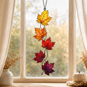 May include: A vertical stained glass suncatcher featuring five maple leaves connected by thin metal stems. The leaves transition in color from yellow at the top to orange, bright red, deep red, and finally a dark purple-red at the bottom.