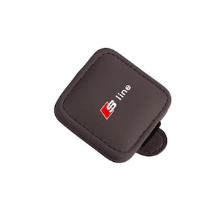 May include: A square, dark brown leather-like coaster or badge with rounded corners and visible stitching along the edges. The centre features the white and red S line logo. A small, matching brown tab extends from the bottom right side of the object.