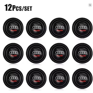 May include: A set of 12 circular black car interior coasters featuring the white Audi logo and the red Audi brand name in the center. Each coaster has a ridged, concentric ring design around the perimeter, providing a textured surface.