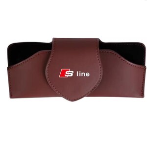 May include: A dark maroon rectangular glasses case with a pointed flap closure. The front of the flap features the white and red Audi S line logo. The interior of the case is lined with black material, and the exterior has visible stitching.