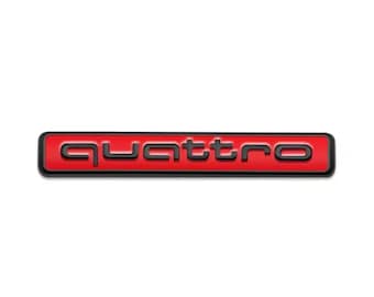 May include: A rectangular emblem with the word "quattro" in black, raised lettering. The background is red, and the border is black. The emblem is set against a white background.