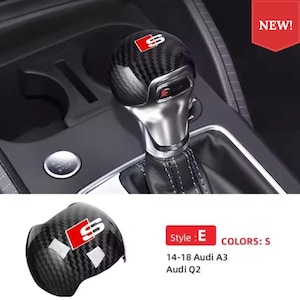 May include: A carbon fibre gear shift knob cover featuring a red and white S logo. The accessory is designed for 14-18 Audi A3 and Audi Q2 models. The top surface displays the S emblem, while the text Style: E and COLORS: S are visible.