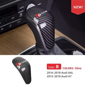 May include: A black carbon fibre gear shift knob cover featuring the S line logo in white and red text. The cover is designed for 2016-2018 Audi A6L and 2015-2018 Audi A7 models. The surface has a textured weave pattern and includes protective film.