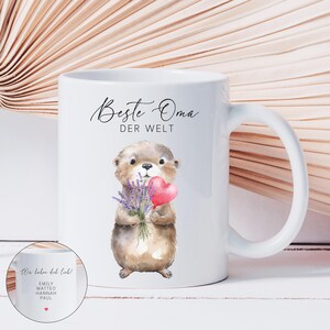 May include: White ceramic mug featuring a watercolor illustration of a brown otter holding a bouquet of lavender and a red heart. The mug has the text "Beste Oma der Welt" and a smaller image with names and a heart.