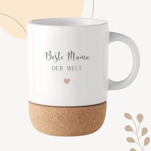 May include: White ceramic mug with a cork base. The mug features the text "Beste Mama DER WELT" in a script font, along with a small pink heart. The mug has a curved handle and is designed for hot beverages.