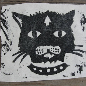 May include: Black and white print of a cat's face on a white fabric background. The cat has a collar with a row of white dots.