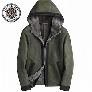 Könnte beinhalten: Grüne Lederjacke mit Kapuze und Fellfutter. Die Jacke hat einen Reißverschluss und schwarze Verzierungen. Das Logo von Jacket Joint, The Leather Factory, befindet sich oben links.