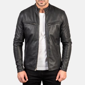 May include: A black leather jacket with a stand-up collar and zippered pockets. The jacket has a front zipper closure and long sleeves. The person in the image is wearing a white t-shirt underneath the jacket and black pants.