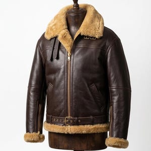 Op de afbeelding: Een donkerbruine leren jas met een beige schapenvachtkraag en voering. De jas heeft een ritssluiting, een tailleband en schapenvachtmanchetten. Gepresenteerd op een houten mannequin.