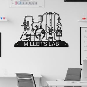 Peut inclure: Une enseigne murale en métal noir représentant une silhouette détaillée de verrerie et d'équipement de laboratoire, incluant des fioles et des tubes. La base affiche le texte MILLER'S LAB en police sans empattement avec deux trous de fixation.