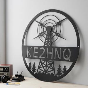 Peut inclure: Décoration murale en métal noir représentant une tour radio avec l'indicatif d'appel KE2HNQ. La pièce circulaire comprend une antenne stylisée, des éclairs et une silhouette de forêt. Une pièce décorative pour un passionné de radio.