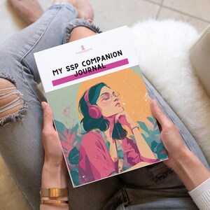 May include: A journal titled "MY SSP COMPANION JOURNAL" held in hands. The cover features an illustration of a person wearing headphones and glasses, with a pink shirt, against a yellow and green background. The person is sitting on a white chair.