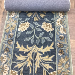 May include: A rectangular runner rug featuring a dark blue central field with a large, symmetrical tan and light green floral and leaf pattern. The rug has a wide border with repeating floral motifs in shades of tan, brown, and light blue.