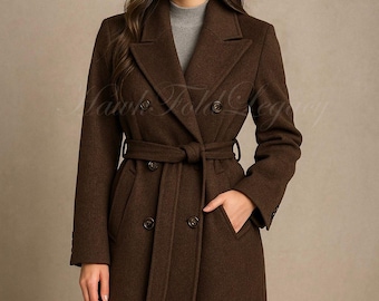 Könnte beinhalten: Ein brauner, zweireihiger Mantel mit passendem Gürtel. Der Mantel hat ein klassisches Design mit großen Knöpfen und Taschen. Das Model trägt einen grauen Rollkragenpullover darunter. Der Mantel ist aus wollähnlichem Material.