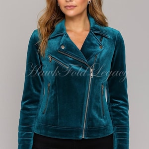 Könnte beinhalten: Türkisblaue Samtjacke mit asymmetrischem Reißverschluss und mehreren Reißverschlusstaschen. Die Jacke hat einen Reverskragen und lange Ärmel mit gerippten Details. Der Text "Hawk Fold Legacy" ist sichtbar.