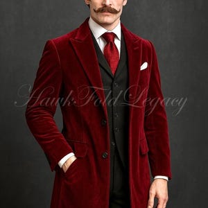 May include: A burgundy velvet overcoat with a black vest and trousers. The coat has a classic lapel, a three-button closure, and pockets. A white pocket square and a red tie complete the look. The image includes the text "Hawk Fold Legacy".