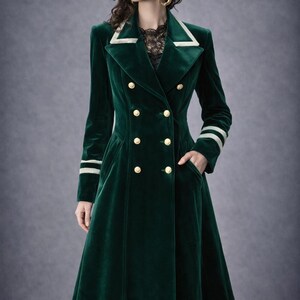 May include: A long, emerald green velvet coat with a double-breasted design and gold buttons. The coat features white trim on the collar and cuffs, and a black lace hemline. The coat has a tailored fit and a classic, elegant style.