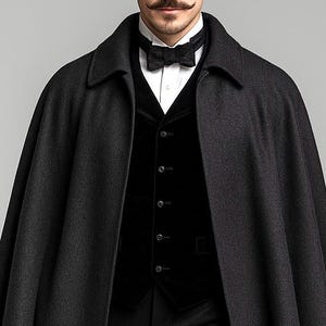 Puede incluir: Una capa de lana gris oscuro sobre un chaleco de terciopelo negro, una camisa blanca de cuello r&iacute;gido y una pajarita negra estampada. La capa presenta un cuello estructurado y cae sobre los hombros, mientras que el chaleco tiene cinco botones.