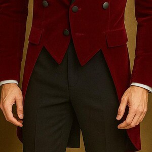 May include: A burgundy velvet tailcoat with black buttons and a notched lapel. The coat has a long, split tail and is paired with black trousers. The sleeves are finished with white cuffs.