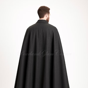 Puede incluir: Una capa de lana gris carb&oacute;n hasta el suelo con un cuello estructurado y un dise&ntilde;o de espalda sin costuras. La prenda cae desde los hombros en una silueta amplia y fluida. El texto Pearland Glam Corner es visible.