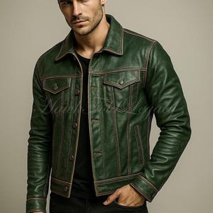 Op de afbeelding: Een groene leren jas met bruine stiksels en knoopsluitingen. De jas heeft twee borstzakken en twee zijzakken. Het model draagt een zwart shirt en een zwarte jeans.