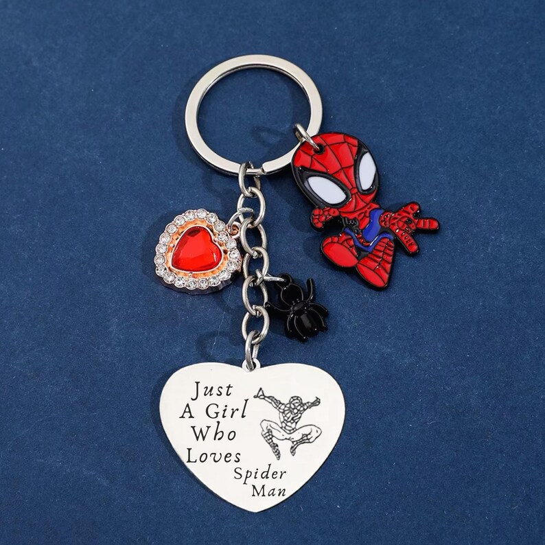 Puede incluir: Un llavero tem&aacute;tico de Spider-Man con una figura de Spider-Man roja y negra, un dije en forma de coraz&oacute;n rojo y un colgante en forma de coraz&oacute;n con el texto "Just A Girl Who Loves Spider Man". El llavero incluye un llavero y una cadena plateados.