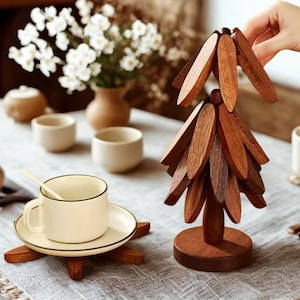 May include: A wooden decorative tree with leaf-shaped pieces, a teacup with a saucer, and a spoon. The teacup and saucer are cream-coloured with a black trim. The tree is made of dark brown wood and sits on a round base.