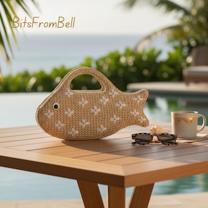 May include: A fish-shaped handbag made of woven beige material with white floral embroidery. The bag has a handle and a single black eye. The bag is on a wooden table with sunglasses and a mug. The text "BitsFromBell" is in the upper left corner.