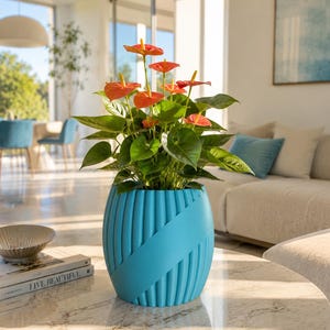 Può includere: Una pianta da interno con fiori arancioni e foglie verdi in un vaso turchese a coste. Il vaso ha una fascia diagonale. La pianta è su un tavolino con piano in marmo. Lo sfondo comprende un divano, sedie e un dipinto.