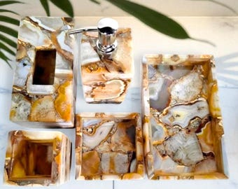Op de afbeelding: Badkameraccessoireset met een natuursteenontwerp. De set bevat een zeepdispenser, een tissuehouder en trays. Een geweven mand bevat witte opgerolde handdoeken.