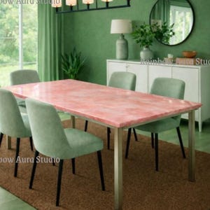 May include: A dining room set featuring a rectangular pink marble table with silver legs, surrounded by four green upholstered chairs. The room has green walls, a brown rug, and a modern chandelier. The text "Rainbow Aura Studio" is visible.