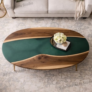 May include: Oval coffee table with a dark wood border and a deep green epoxy resin center. The table has gold-colored legs and a tray with flowers on top. The table is approximately 50 inches long.