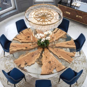 Puede incluir: Vista aérea de un comedor de lujo con una gran mesa redonda de madera. La mesa está rodeada por ocho sillas de terciopelo azul marino. Una gran lámpara de araña adornada cuelga sobre la mesa, y una alfombra está debajo. La mesa tiene unos 200 cm de diámetro.