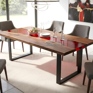 Può includere: Un tavolo da pranzo rettangolare in legno con intarsio in resina rossa. Il tavolo ha gambe in metallo nero ed è circondato da sedie imbottite grigie. Il tavolo è apparecchiato con piatti, bicchieri e posate. La stanza ha un design moderno.