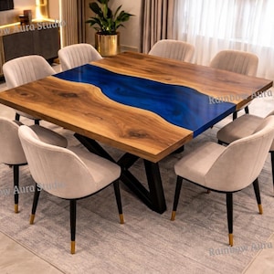 Puede incluir: Una gran mesa de comedor de madera con un diseño de río de resina azul, rodeada de ocho sillas tapizadas. La mesa tiene una base de metal oscuro y está sobre una alfombra de color claro. Las sillas tienen patas negras con puntas doradas.