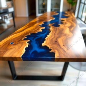Op de afbeelding: Een rechthoekige houten tafel met een rivier van blauwe hars in het midden. Het hout heeft een warme, bruine tint met natuurlijke nerfpatronen. De tafel wordt ondersteund door zwarte metalen poten. De tafel is ongeveer 180 cm lang.
