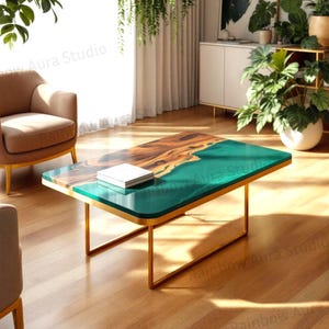 May include: A rectangular coffee table with a wooden top and a teal resin inlay. The table has a gold-colored metal frame and legs. A white book sits on the table. The table is in a living room setting.