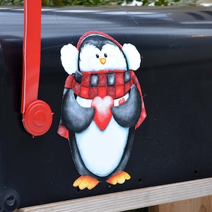 May include: A black mailbox with a red flag and a penguin sticker. The penguin is wearing a red and black scarf and holding a red heart. The mailbox has the text "U.S. MAIL" and "APPROVED BY THE POSTMASTER GENERAL" on it.