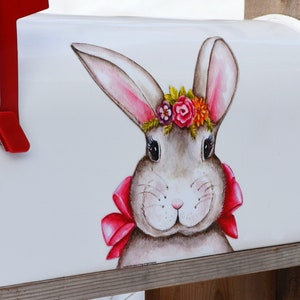 May include: White mailbox with a painted image of a grey bunny wearing a pink bow and a flower crown. The bunny is looking directly at the viewer.